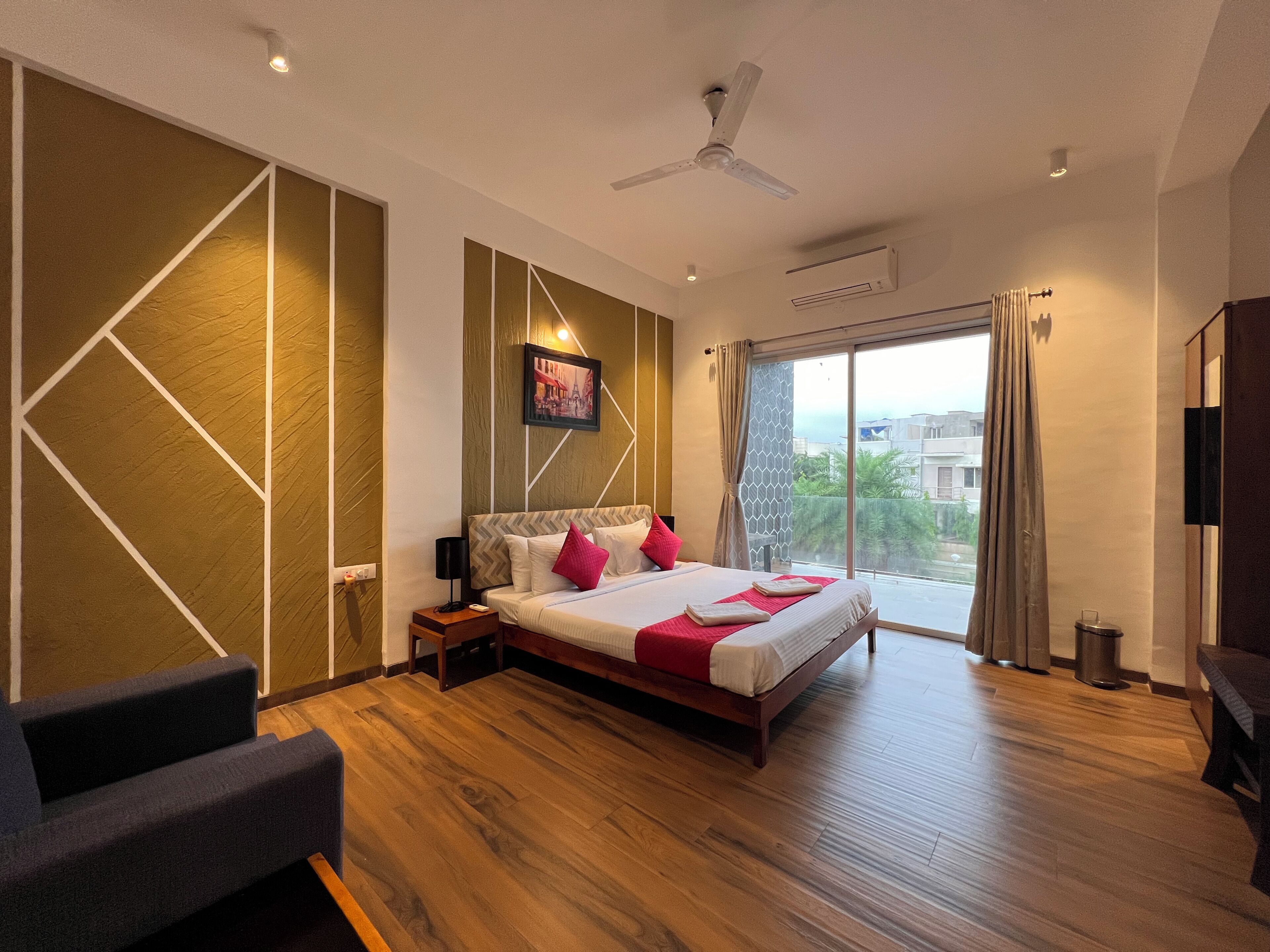 Une chambre d’hôtel moderne dotée d’un grand lit, d’un ventilateur de plafond, d’une vue sur la ville par la fenêtre et d’un plancher en bois.