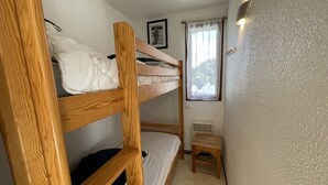 A bunk bed room with a small wooden stool and a window with curtains. - Functional apartment near slopes, ideal for 4-6 people (Le Lioran)
