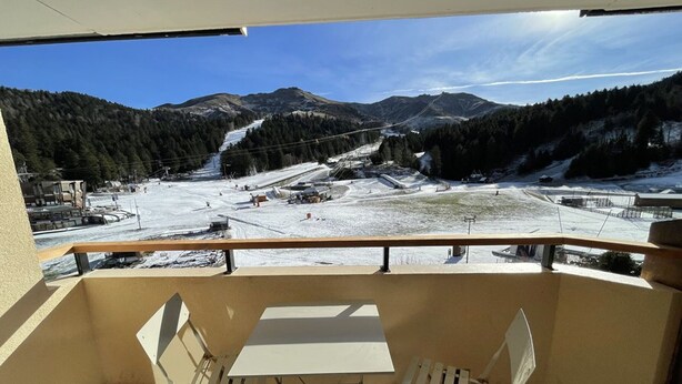 A balcony with a table and chairs, overlooking a snowy mountain area with a ski slope. - Functional apartment near slopes, ideal for 4-6 people (Le Lioran)