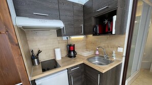 A compact kitchen with dark wood cabinets, a small refrigerator, a coffee maker, and a sink. - Functional apartment near slopes, ideal for 4-6 people (Le Lioran)