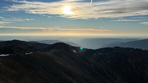 Eine gebirgige Landschaft mit klarem Himmel und untergehender oder aufgehender Sonne.