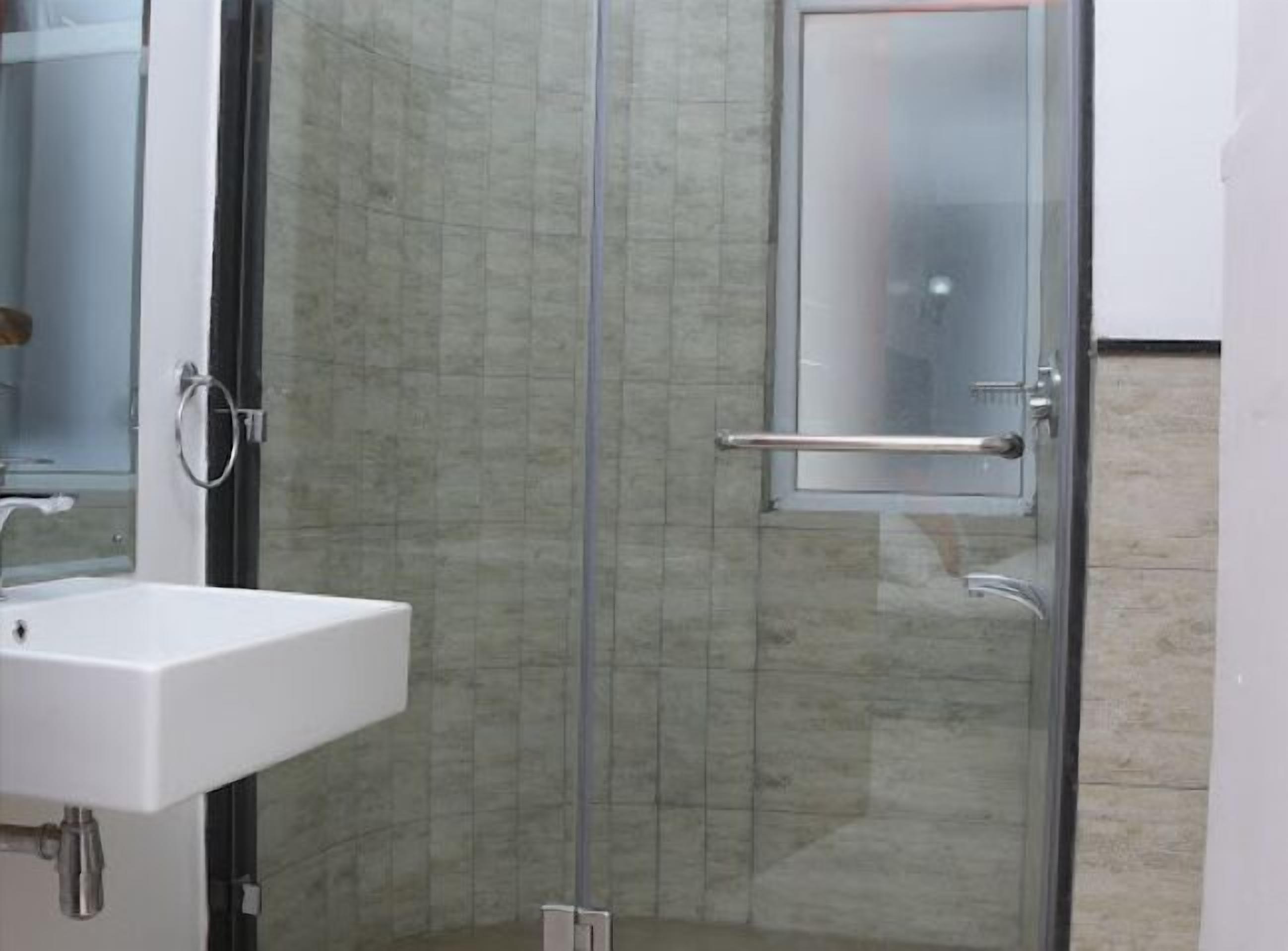 Een badkamer met een douchecabine van glas, een witte wastafel en een spiegel.
