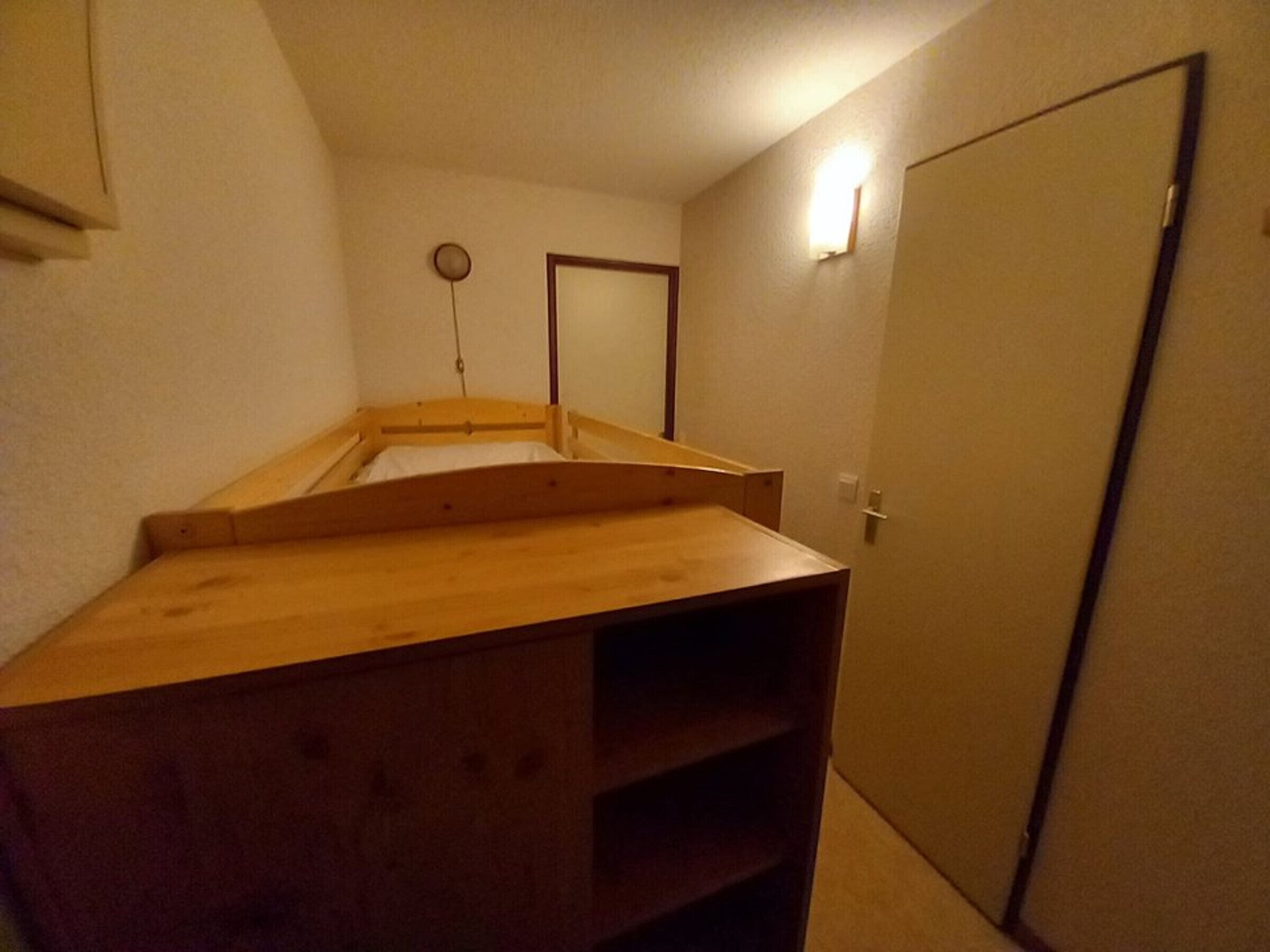 Un petit espace composé d’une seule pièce, avec un lit superposé en bois, une porte et un luminaire fixé au mur.