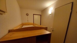 A small, single-room layout with a wooden bunk bed, a door, and a wall-mounted light fixture. - Studio cabin with southeast balcony in Le Lioran (Le Lioran)