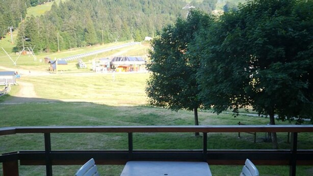 A table and two chairs on a wooden deck with a view of a rural landscape, including a road and buildings in the distance. - Studio cabin with southeast balcony in Le Lioran (Le Lioran)