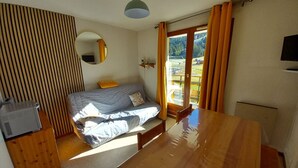 A compact bedroom with a bed, a wooden table, a small desk, a mirror, and a window with curtains. - Studio cabin with southeast balcony in Le Lioran (Le Lioran)