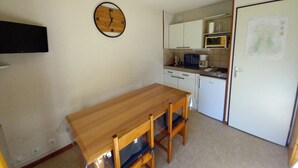 A small kitchen with a wooden table and chairs, a clock on the wall, and a microwave. - Studio cabin with southeast balcony in Le Lioran (Le Lioran)