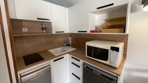 Ett kompakt kök med vita skåp, en mikrovågsugn, en diskmaskin och en bänkskiva i trä.