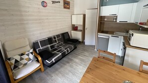 Ett kompakt bostadsutrymme med en soffa, ett matbord, ett litet kök och ett litet kylskåp.