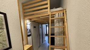En smal hall med en träkonstruerad loftssäng och ett litet träskåp.