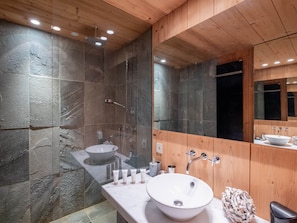 A modern bathroom with a stone wall, a large mirror, a wooden ceiling, and a white sink. - Spacious apartment, panoramic view (Villard-sur-Doron)