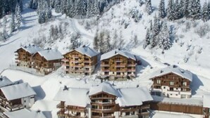 Un ensemble de bâtiments de style chalet en bois, dotés de nombreux balcons, entourés d’arbres couverts de neige et situés à proximité d’une piste de ski.