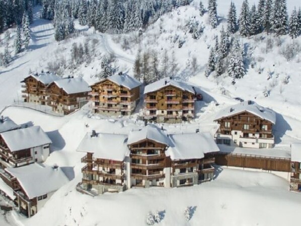 A cluster of wooden chalet-style buildings with multiple balconies, surrounded by snow-covered trees and a ski slope. - Spacious apartment, panoramic view (Villard-sur-Doron)