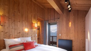 Une pièce aux murs lambrissés, avec un grand lit, une vue sur l’extérieur par une porte et un radiateur.