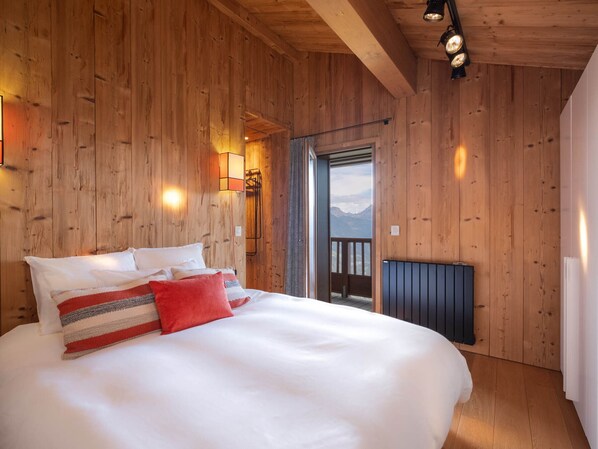 Une pièce aux murs lambrissés, avec un grand lit, une vue sur l’extérieur par une porte et un radiateur.