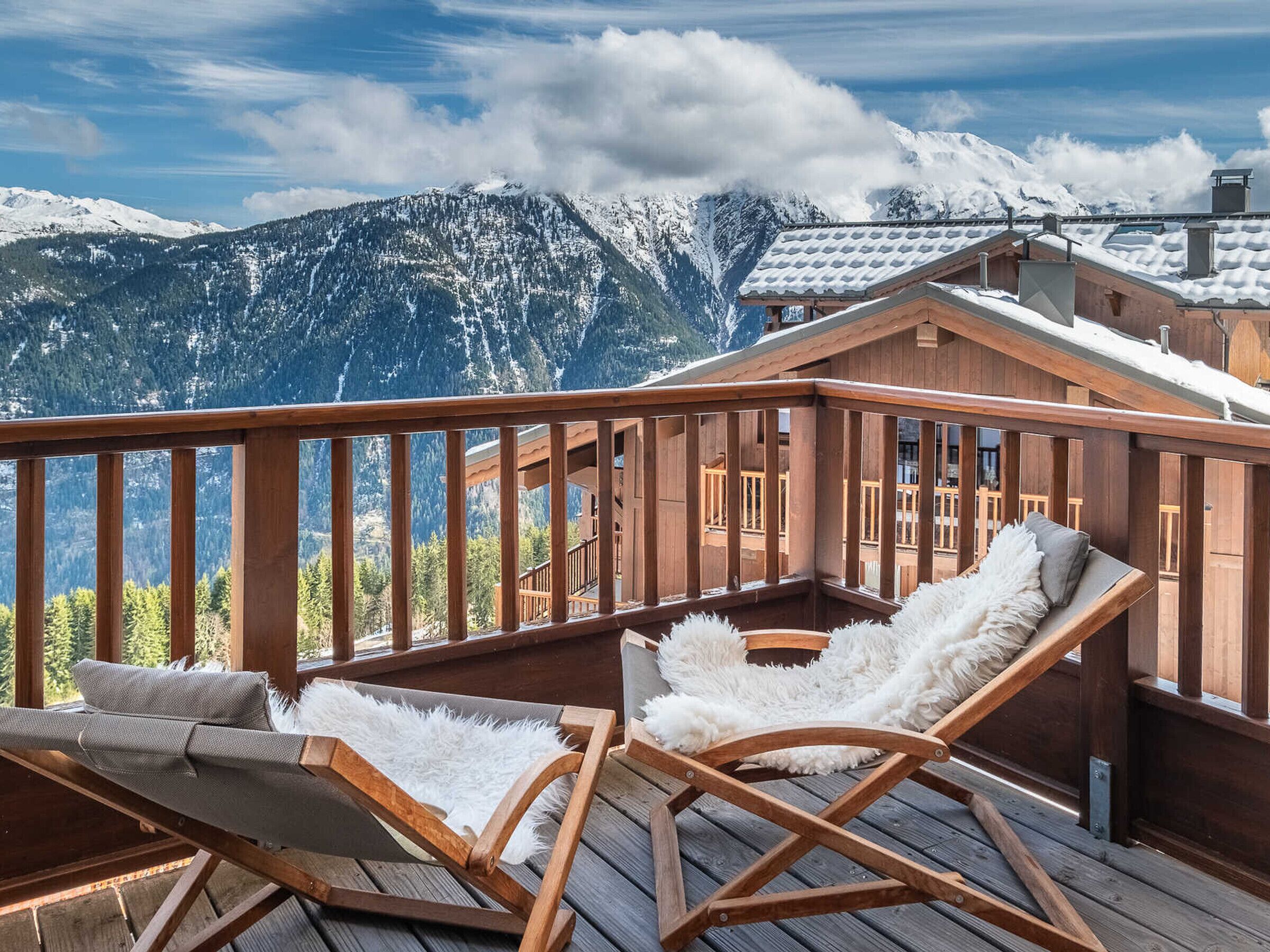 Eine Holzterrasse mit zwei Liegestühlen und Blick auf schneebedeckte Berge.