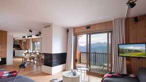 Un salon moderne doté d’un grand téléviseur à écran plat, d’une cheminée chaleureuse et d’un balcon offrant une vue sur les montagnes.