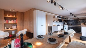 Une cuisine moderne avec une table à manger en bois, des chaises blanches et un plan de travail noir.