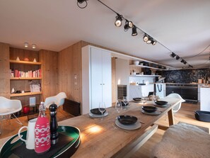 A modern kitchen with a wooden dining table, white chairs, and a black countertop. - Spacious apartment, panoramic view (Villard-sur-Doron)
