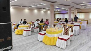 A banquet hall with round tables, white and yellow tablecloths, and guests seated. - Hotel Rekha International (Rajgir)