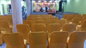 A church interior with rows of yellow chairs, a stage with floral decorations, and a large pillar. - Hotel Rekha International (Rajgir)