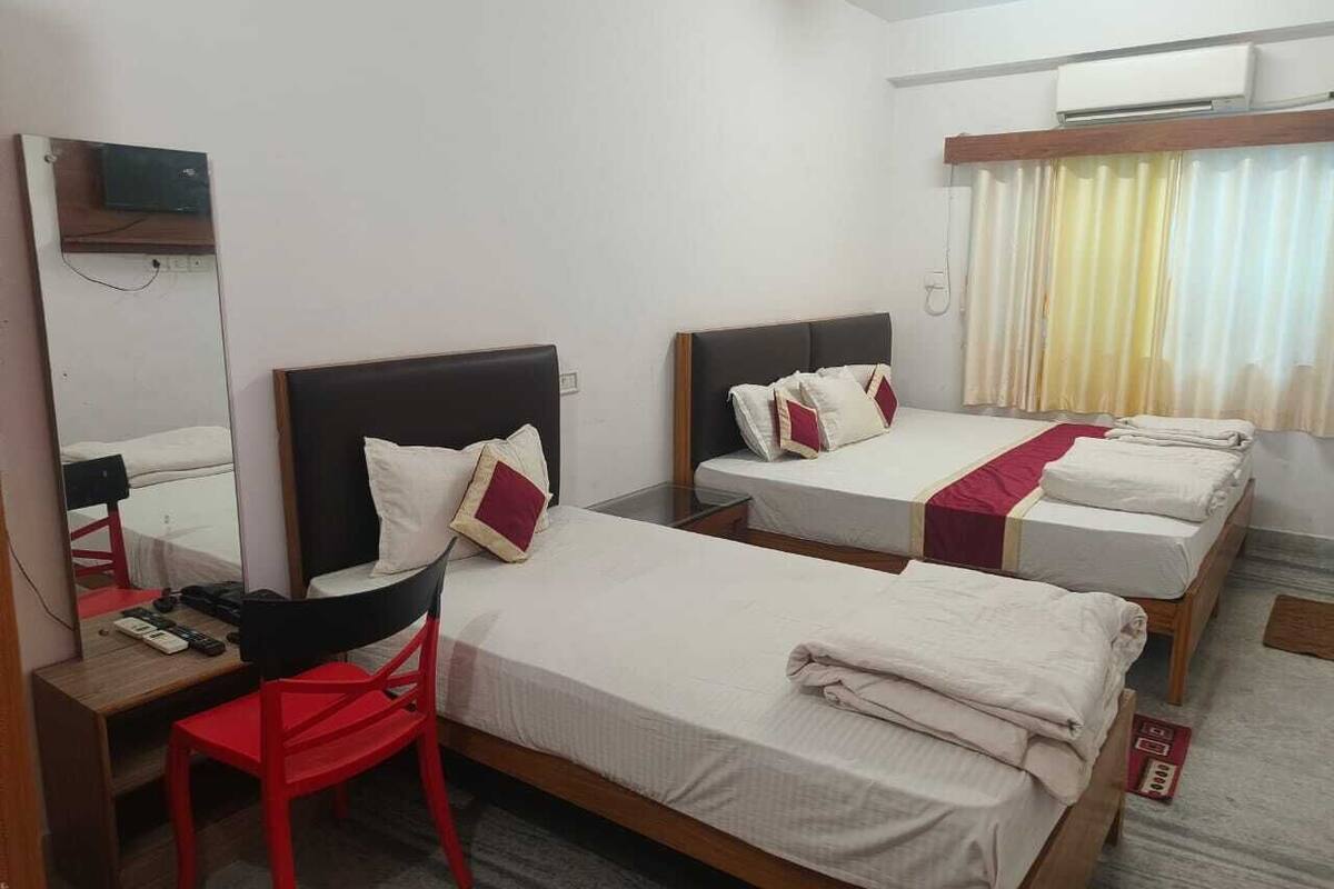 A hotel room with three beds, a desk, a chair, and a mirror.