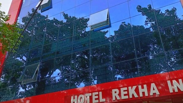 A modern building with a reflective glass facade, a prominent red and white sign indicating a restaurant and banquet facility, and a visible entrance with a parking sign. - Hotel Rekha International (Rajgir)