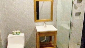 A bathroom with a toilet, a sink with a wooden stool, a mirror, and a glass shower enclosure.