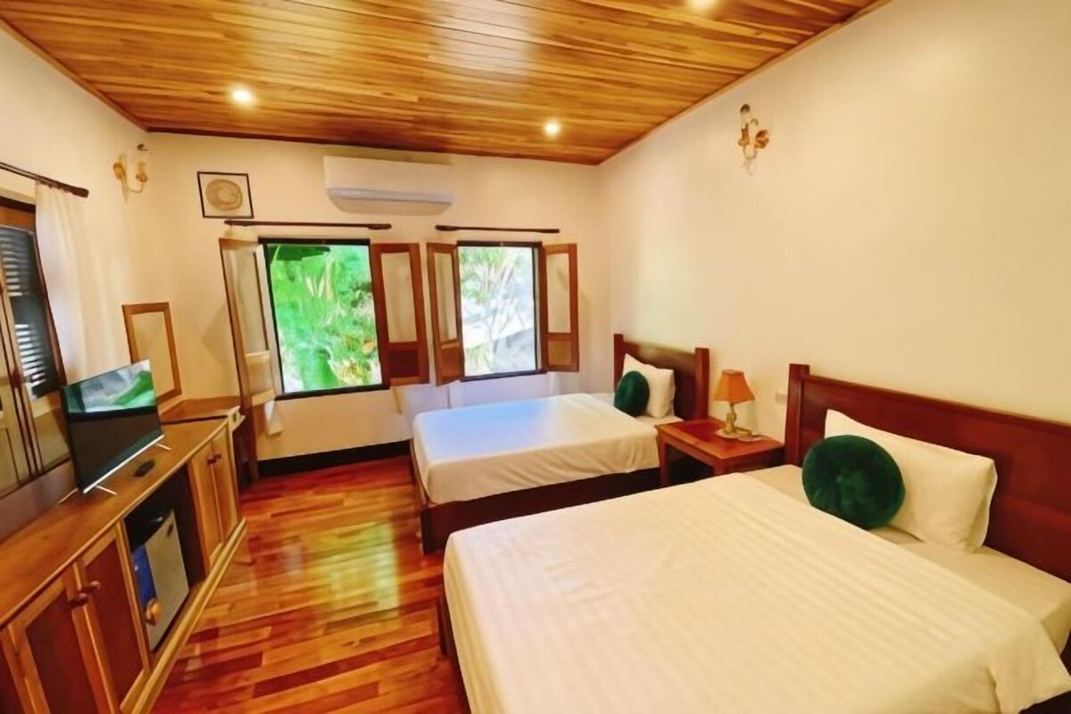 Habitación de hotel con dos camas, techo de madera, televisión y ventana con vista a zonas verdes.