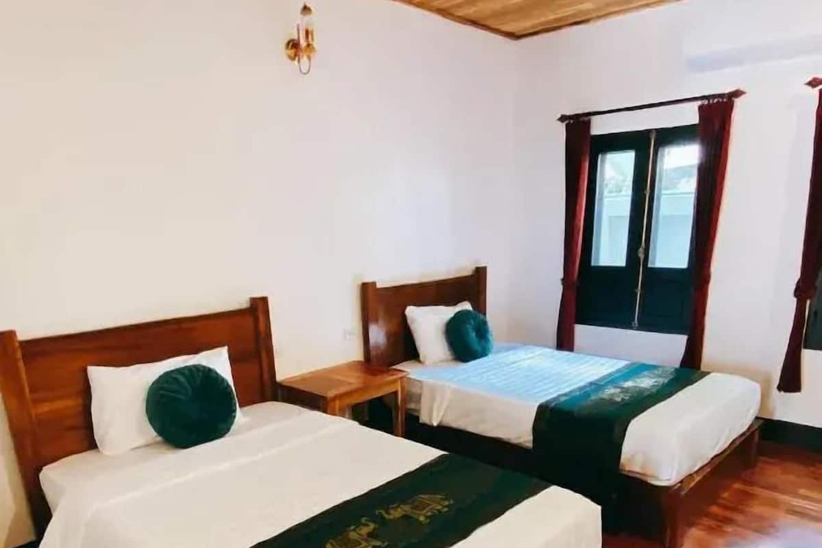 A hotel room with two wooden beds, a wooden ceiling, and a window with curtains.