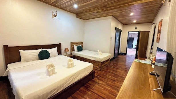 A hotel room with two beds, wooden flooring, a flat-screen TV, and a wooden ceiling.