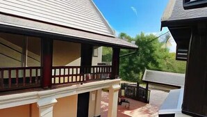 A covered outdoor area with a tiled floor, a balcony with a railing, and a building with a sloped roof.
