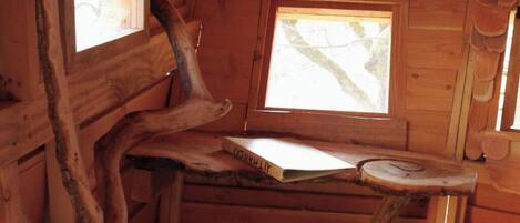 L’intérieur d’un chalet en bois, au décor rustique, avec une fenêtre et une table en bois sur laquelle repose un livre.