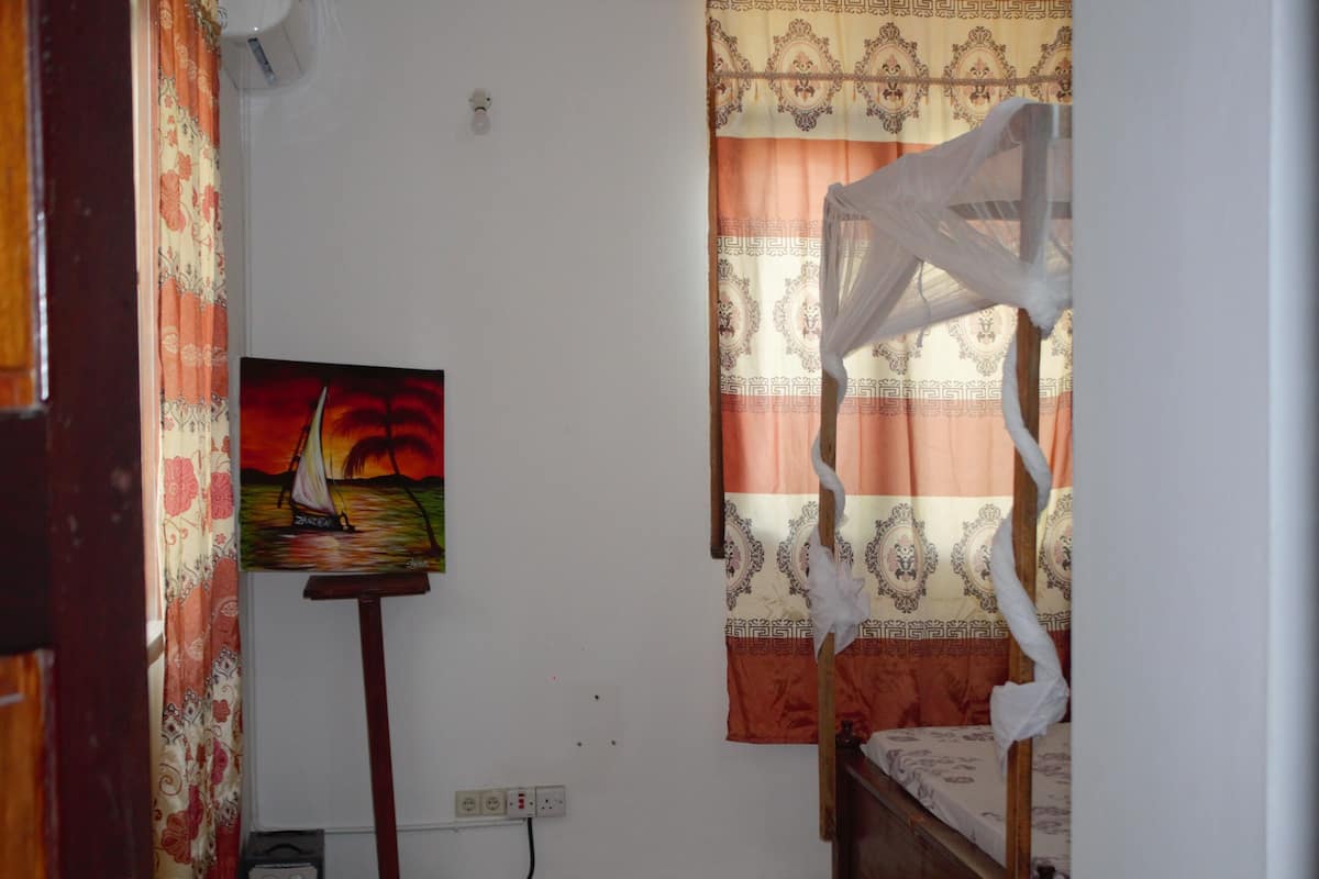Une chambre à coucher avec un lit, un tableau au mur, un rideau et une fenêtre ornée d’un rideau à motifs.
