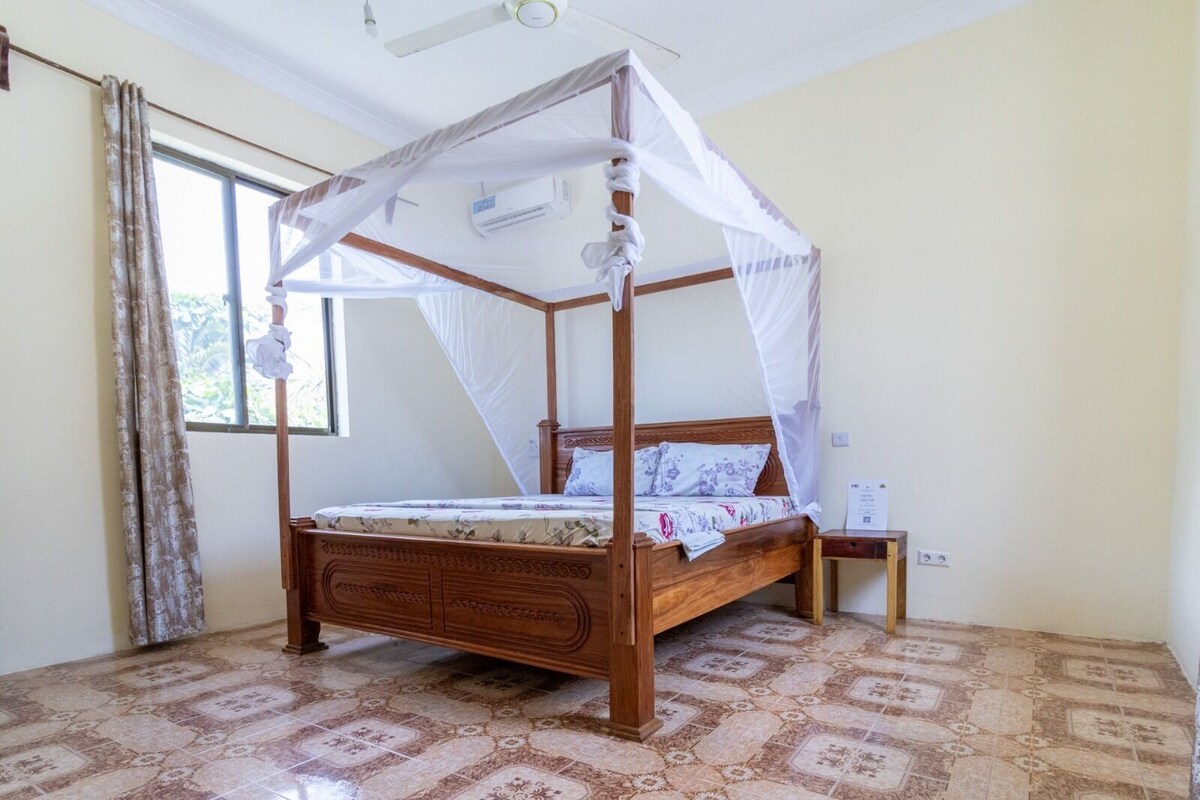 Una cama con dosel, una mesita de noche y una ventana con cortinas.