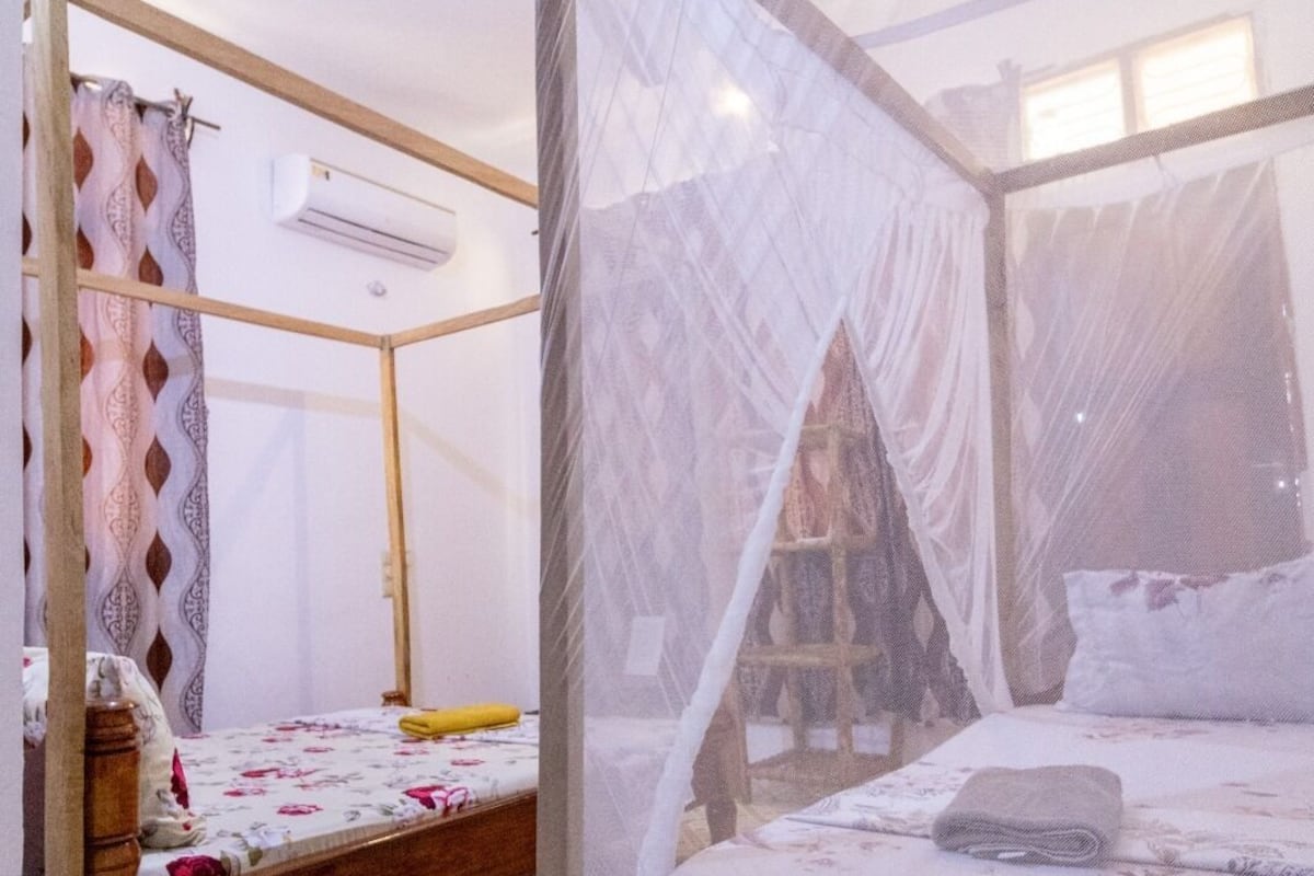 Une chambre avec un lit recouvert d’une moustiquaire, un cadre de lit en bois, un sol à motifs et un appareil de climatisation.