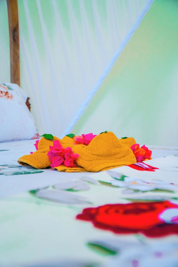 A bed with a floral-patterned bedspread and a yellow towel with pink flowers.