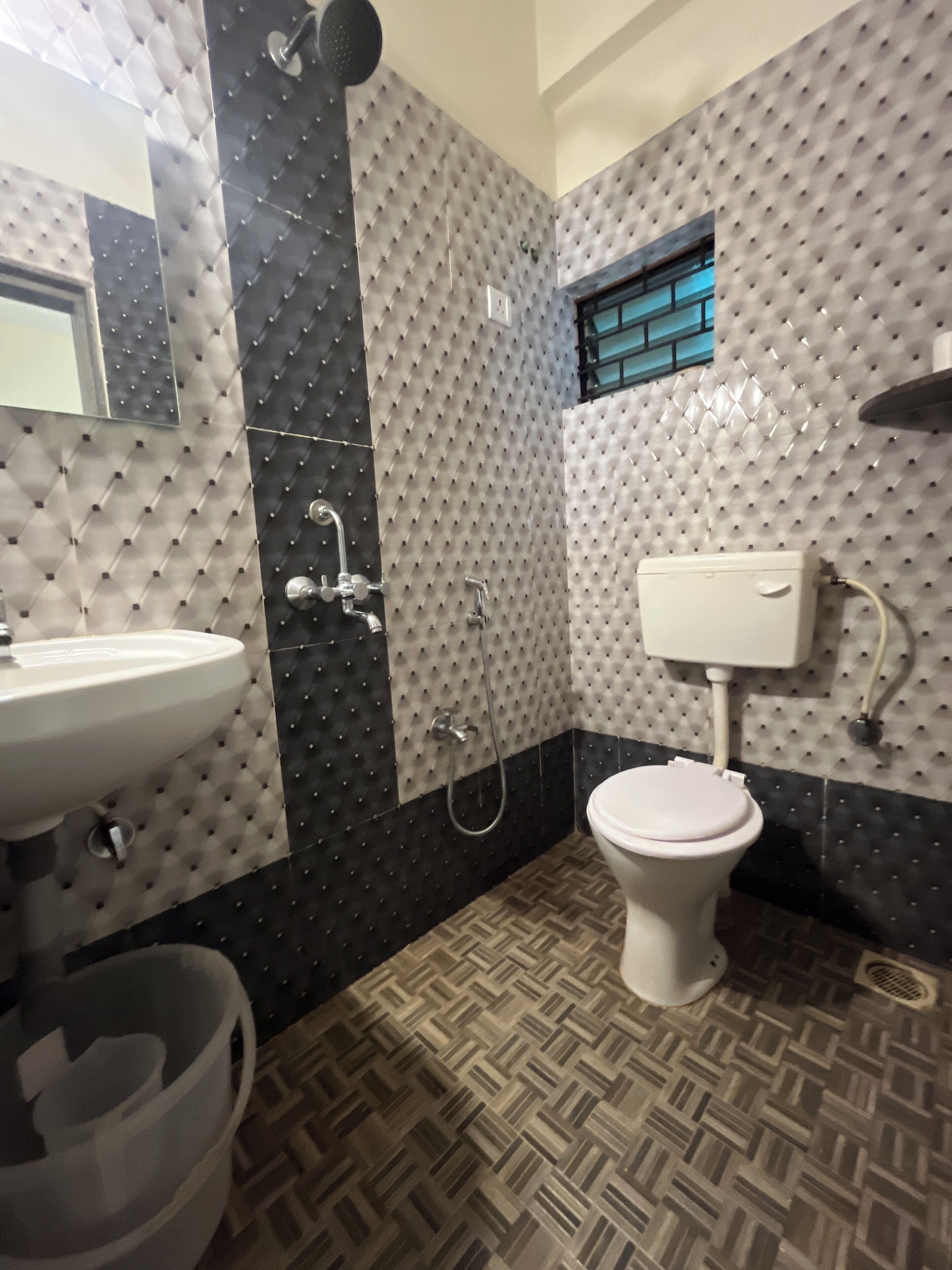 Un baño con lavamanos, inodoro y ducha blancos. Las paredes tienen un patrón de rombos y el piso un diseño en espiga.