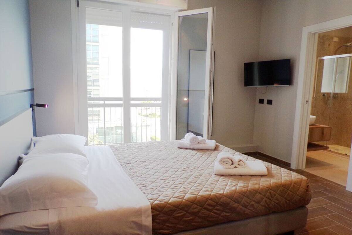 A hotel room with a bed, a TV mounted on the wall, and a bathroom visible through an open door.
