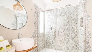 Une salle de bain moderne avec un lavabo rond, un miroir et une douche dotée d’une porte en verre à motifs.