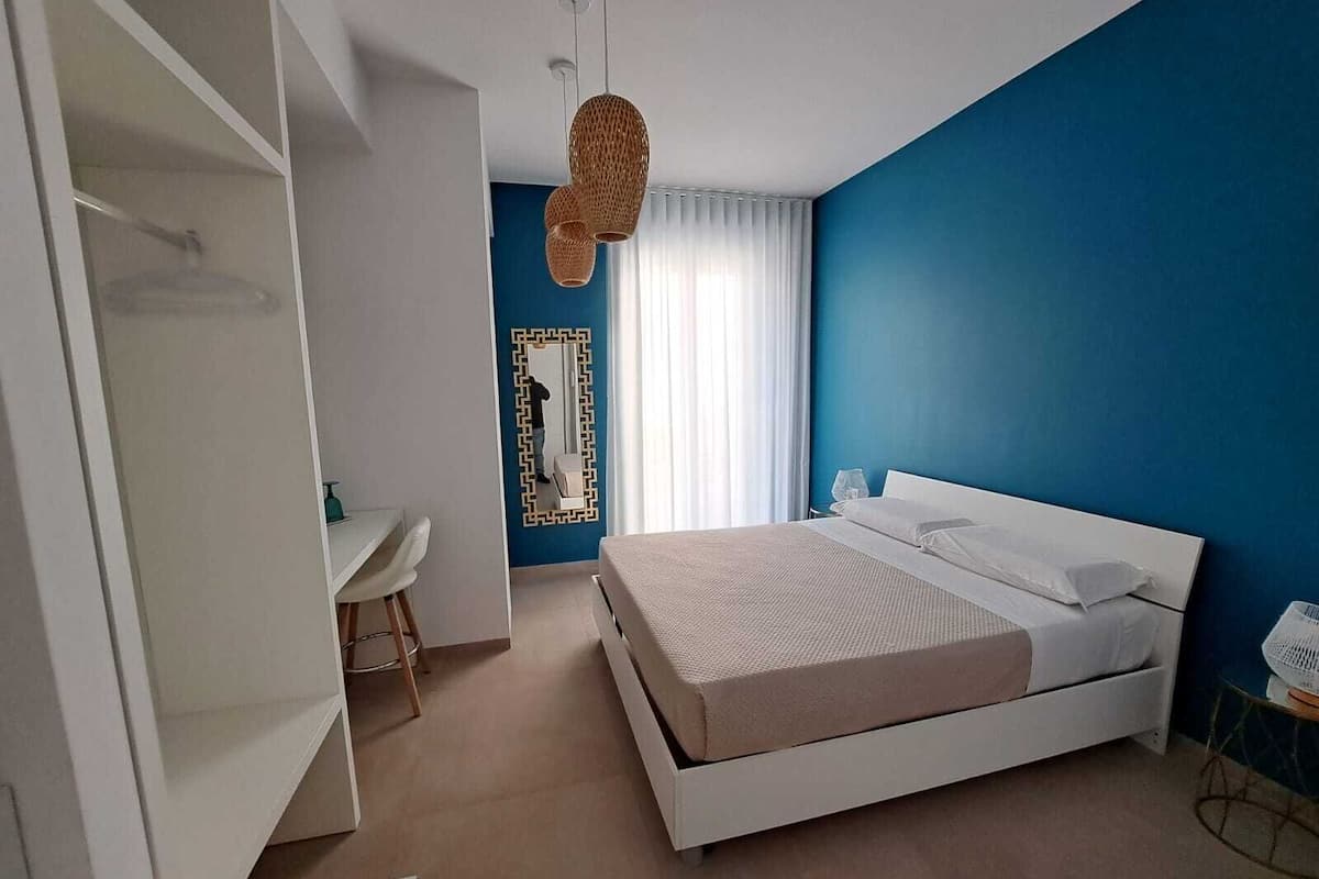 A modern bedroom with a white bed, a desk, and a wardrobe.