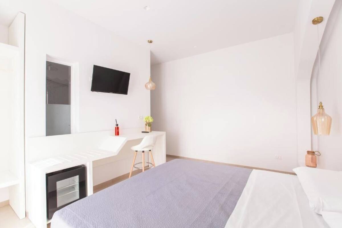 A modern hotel room with a bed, a desk, a chair, a TV, and a small table with a vase.