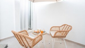 Un balcon avec des fauteuils en osier, une petite table ronde sur laquelle sont disposés des aliments pour le petit-déjeuner, et un grand parasol.