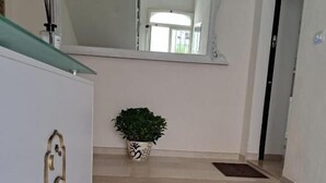 Un escalier menant à une pièce où se trouve un grand miroir au-dessus d’une console, une plante en pot et un luminaire fixé au mur.