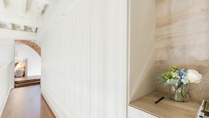 A hallway with a wooden floor, white walls, and a brick archway leading to a room. A vase with flowers is on a shelf. - Cortile Moderno Apartment (Lucca)