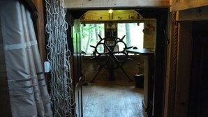 Un intérieur en bois agrémenté d’un grand volant de navire, d’un plancher en bois rustique et d’une fenêtre donnant sur la forêt.