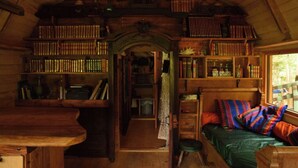 L’intérieur chaleureux d’un chalet avec un plafond en bois, des étagères intégrées, un lit agrémenté de coussins colorés et un petit tabouret.