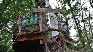 Une cabane en bois perchée dans un arbre, avec une pancarte sur laquelle on peut lire « ATLANTIDE ».