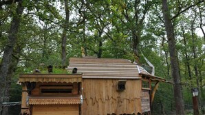 Une cabane en bois rustique, dotée d’un toit en pente et d’un petit balcon, entourée d’arbres.