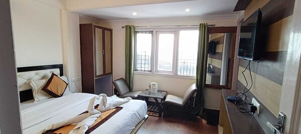 A hotel room with a bed, a desk, a chair, a TV, and a window with curtains.
